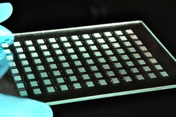 Glasplatte mit regelmäßigem Array mikrooptischer Strukturen, gehalten von einer behandschuhten Hand im Labor – hergestellt mittels Nanoimprint-Lithographie für optische und photonische Anwendungen.