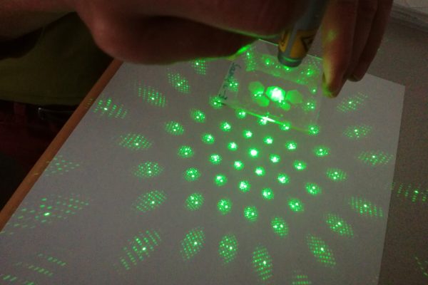 Laserlicht trifft auf nanostrukturierte optische Oberfläche und erzeugt Beugungsmuster – Demonstration eines nanooptischen Bauteils hergestellt mittels Nanoimprint-Lithographie.